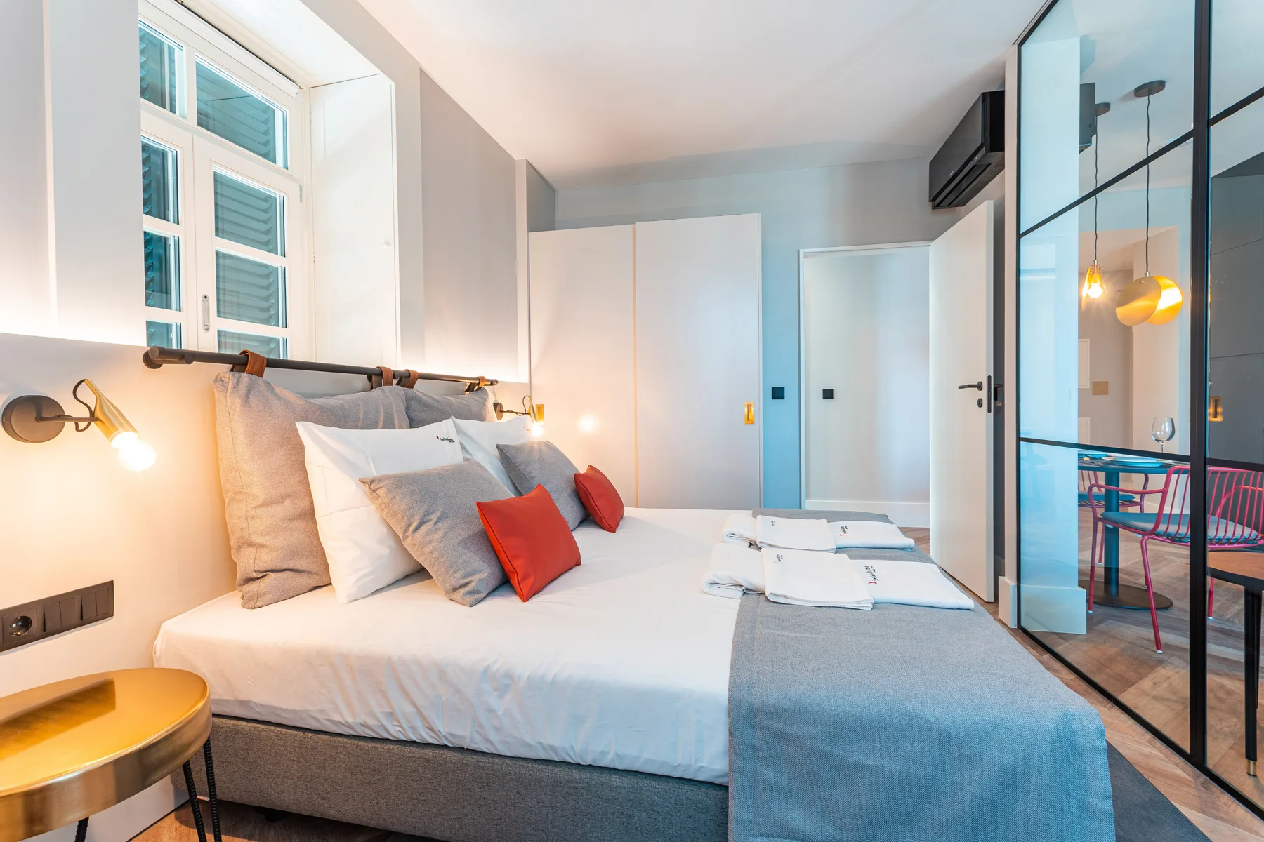 A bright bedroom with a neatly made bed and glass doors opening to a dining area.
