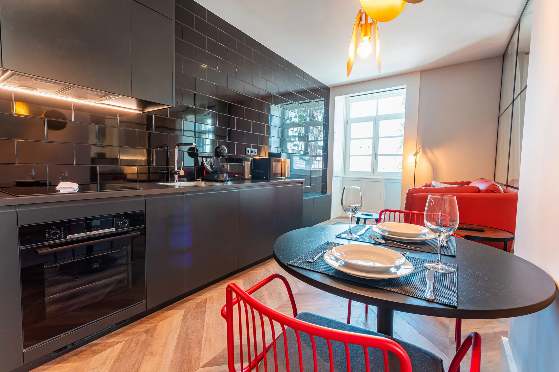 An open-plan kitchen and dining area with a table beside a red sofa.