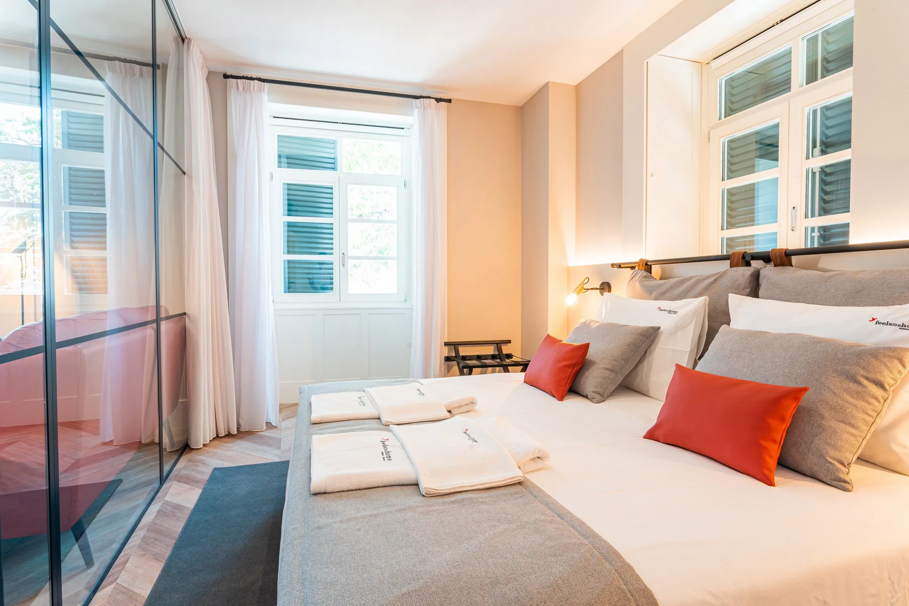A bright bedroom with a bed, red cushions, and large windows.