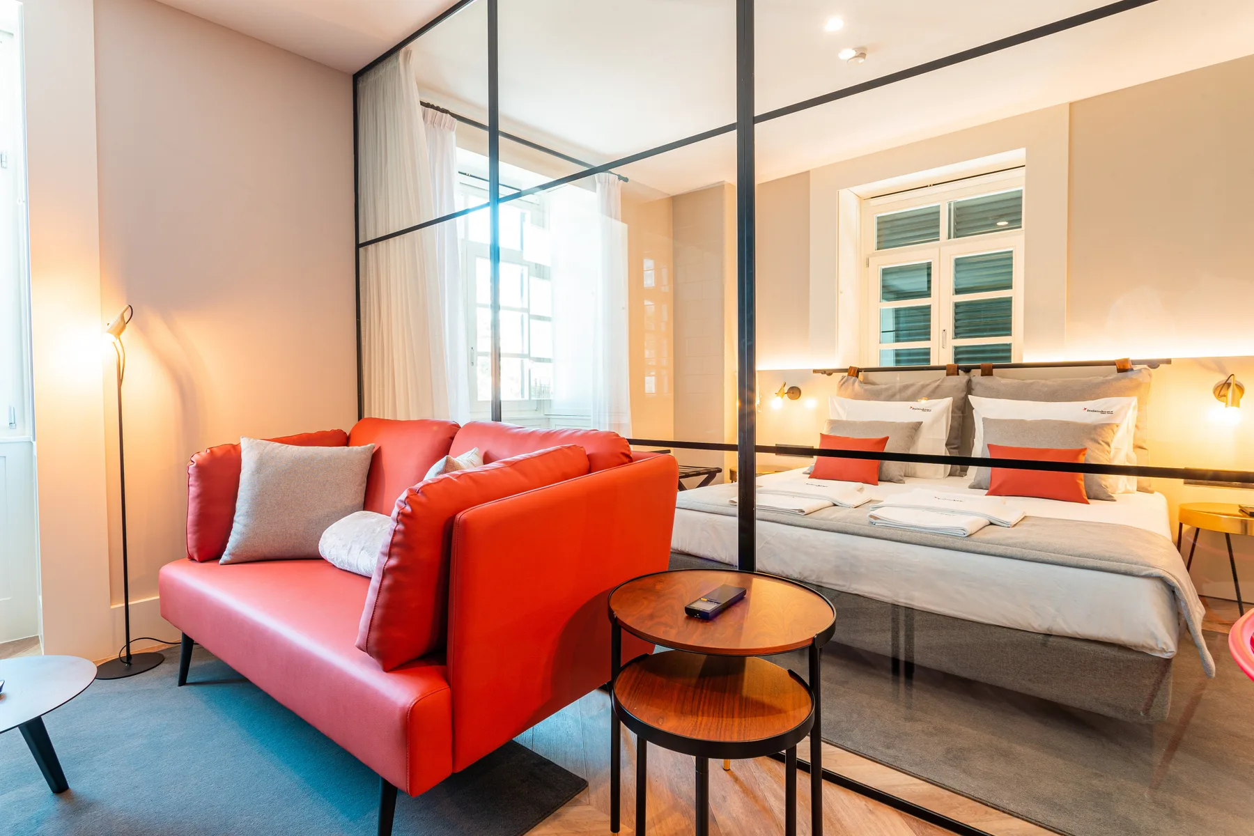 A bedroom with a bed and red seating beside a glass partition.