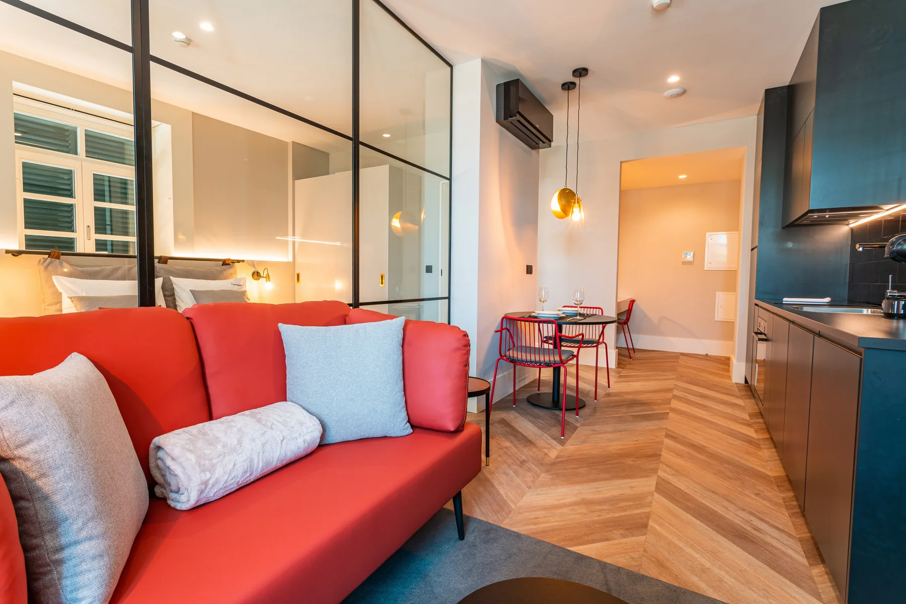 An open-plan living area with red seating, a dining table, and a kitchen.