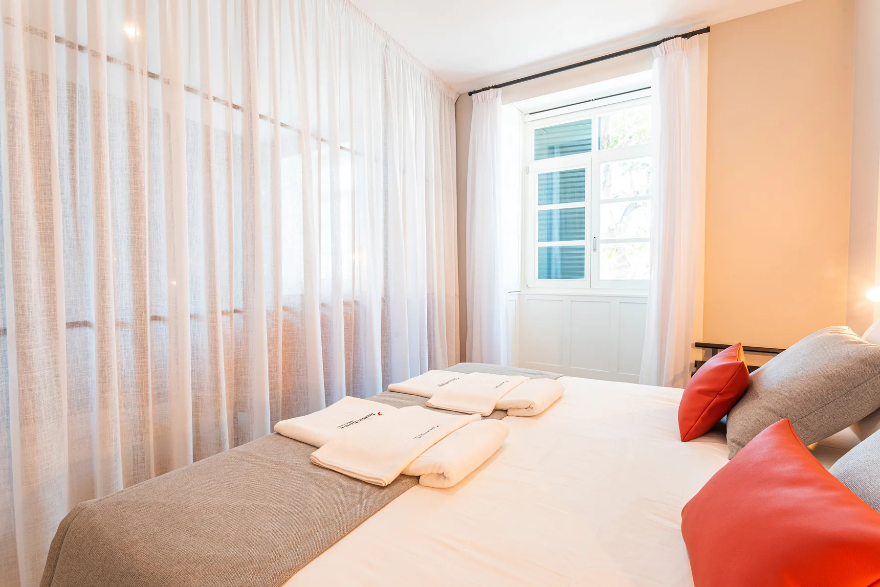 A bright bedroom with a neatly made bed and sheer curtains.