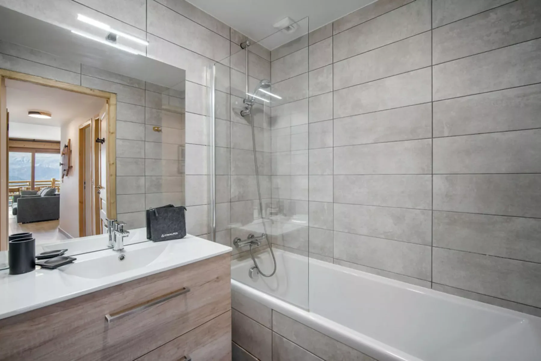 Un baño alicatado con bañera y lavabo bajo un espejo grande.