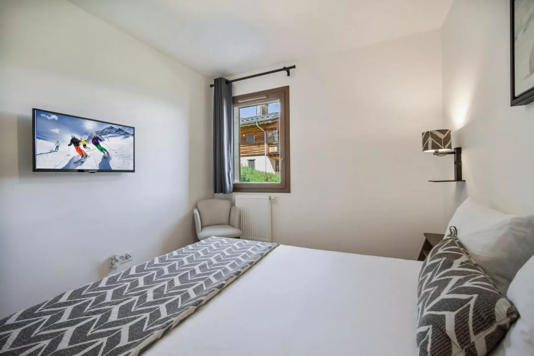 Un dormitorio con una cama, una ventana y un televisor montado en la pared.