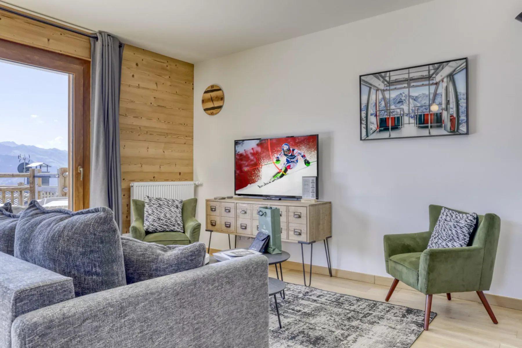 A living room with gray seating, green armchairs, and framed artwork.