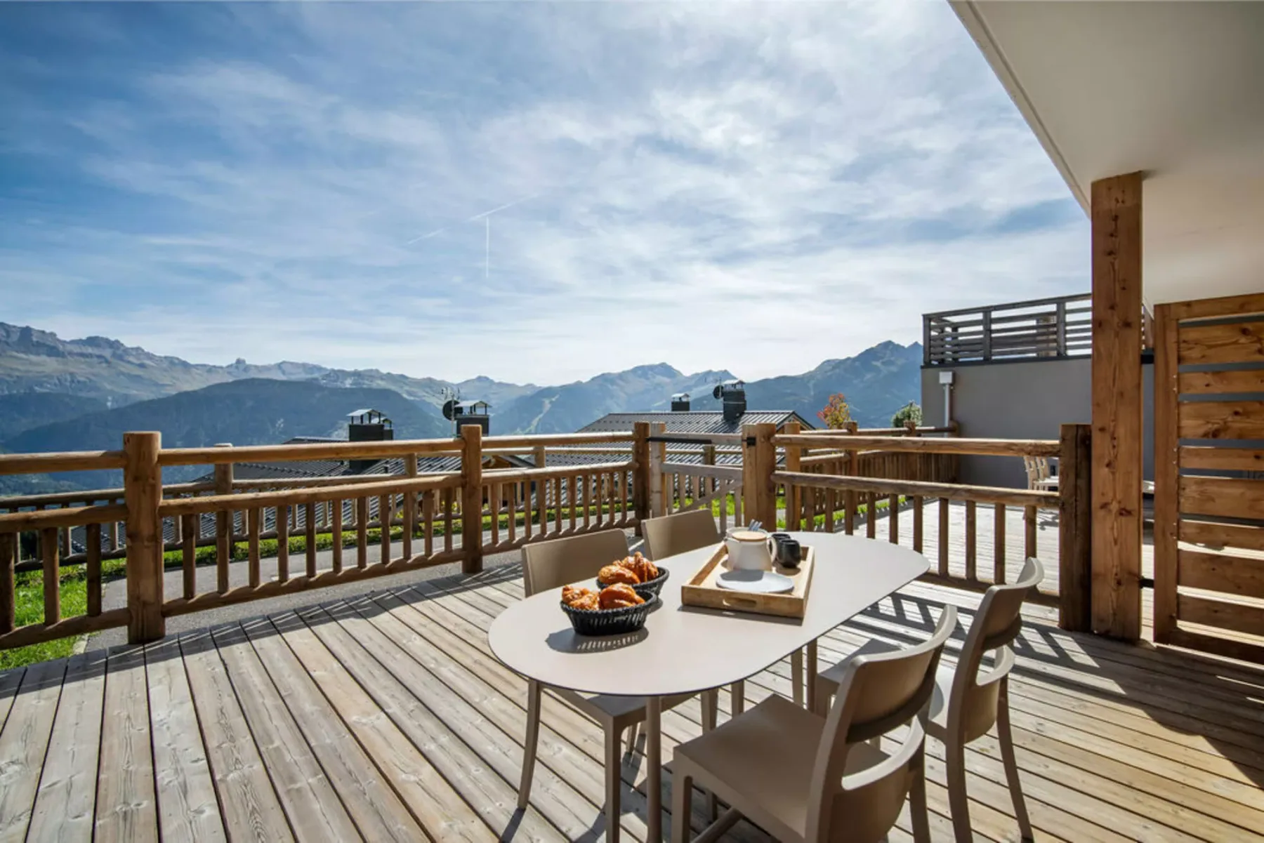 Una terraza de madera con muebles de comedor exterior tiene vistas a una cordillera.