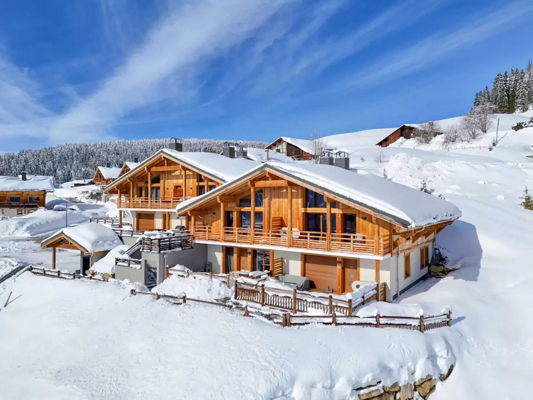 Chalés de madera se encuentran en un paisaje montañoso cubierto de nieve bajo un cielo azul.