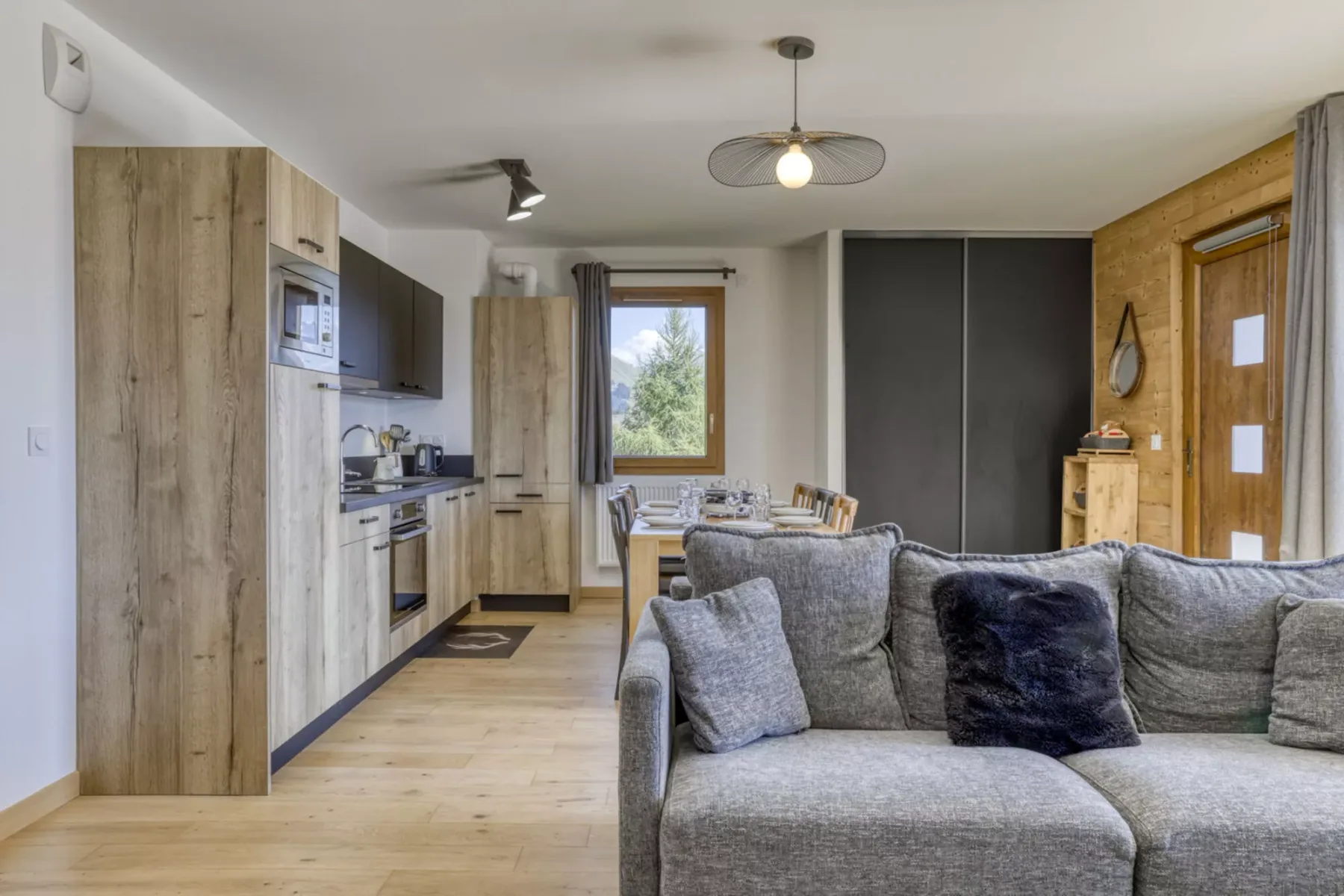 Una sala se abre a una cocina compacta, con una amplia zona de asientos grises en primer plano.