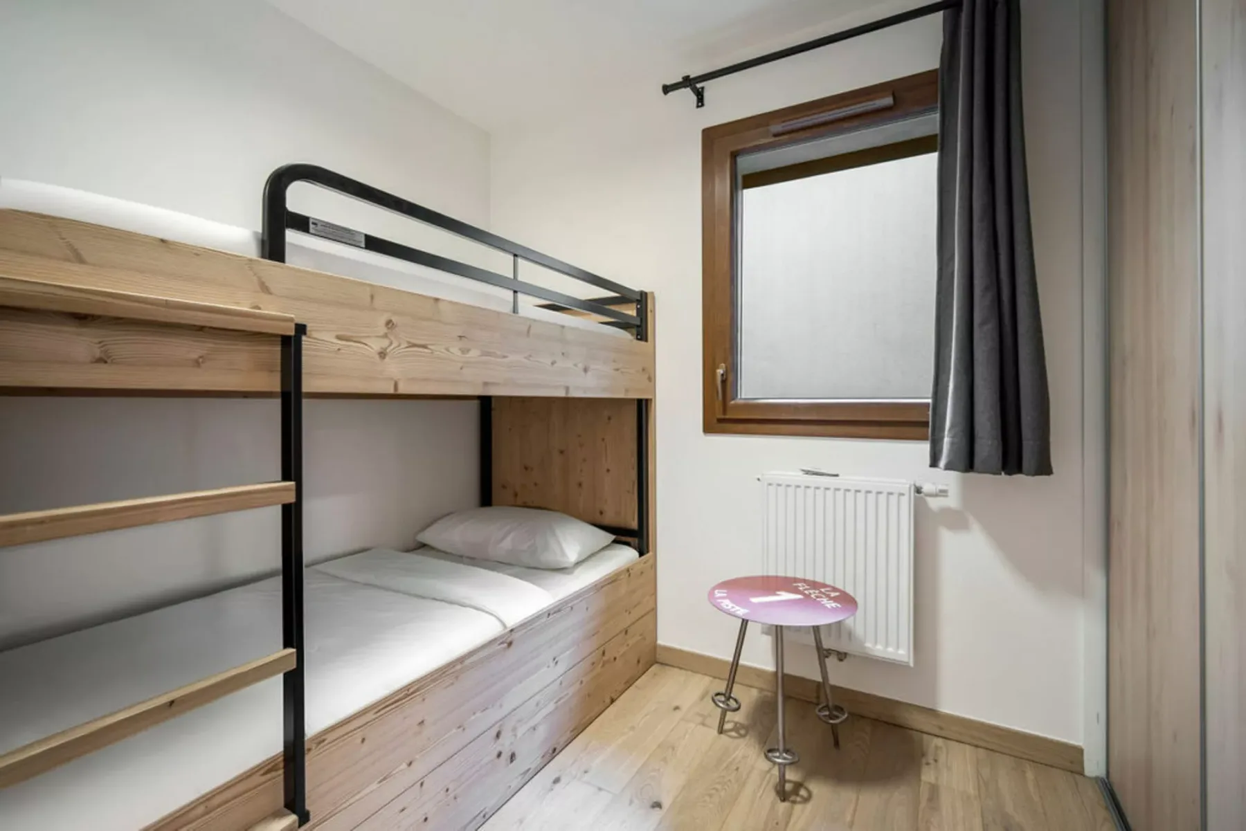 Un dormitorio compacto con una litera de madera, una ventana y una mesita.