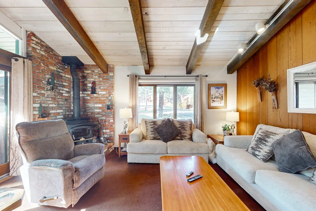 A living room with comfortable seating, exposed ceiling beams, and a brick fireplace.