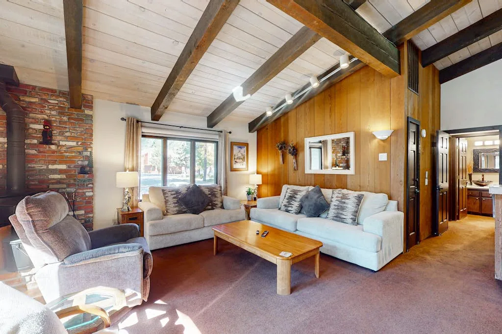 A living room with seating arranged around a wooden coffee table beneath exposed ceiling beams.
