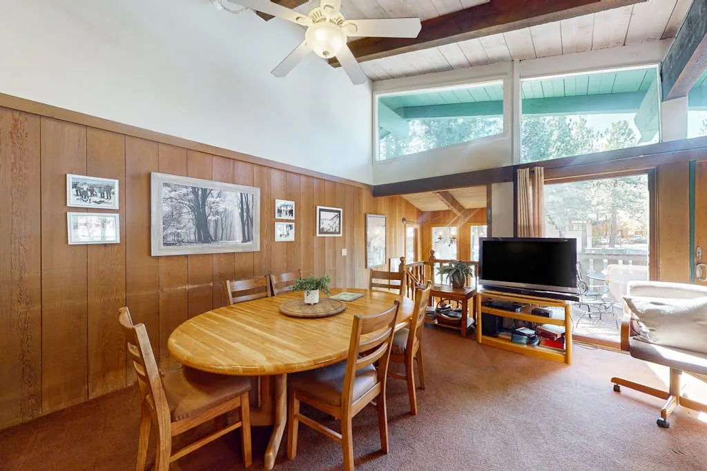 A wood-paneled living room has a dining table and television beside large windows.