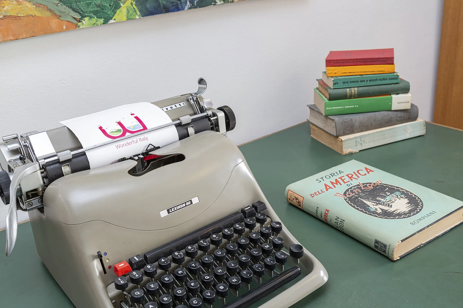 Una máquina de escribir antigua y unos libros están sobre una mesa verde.