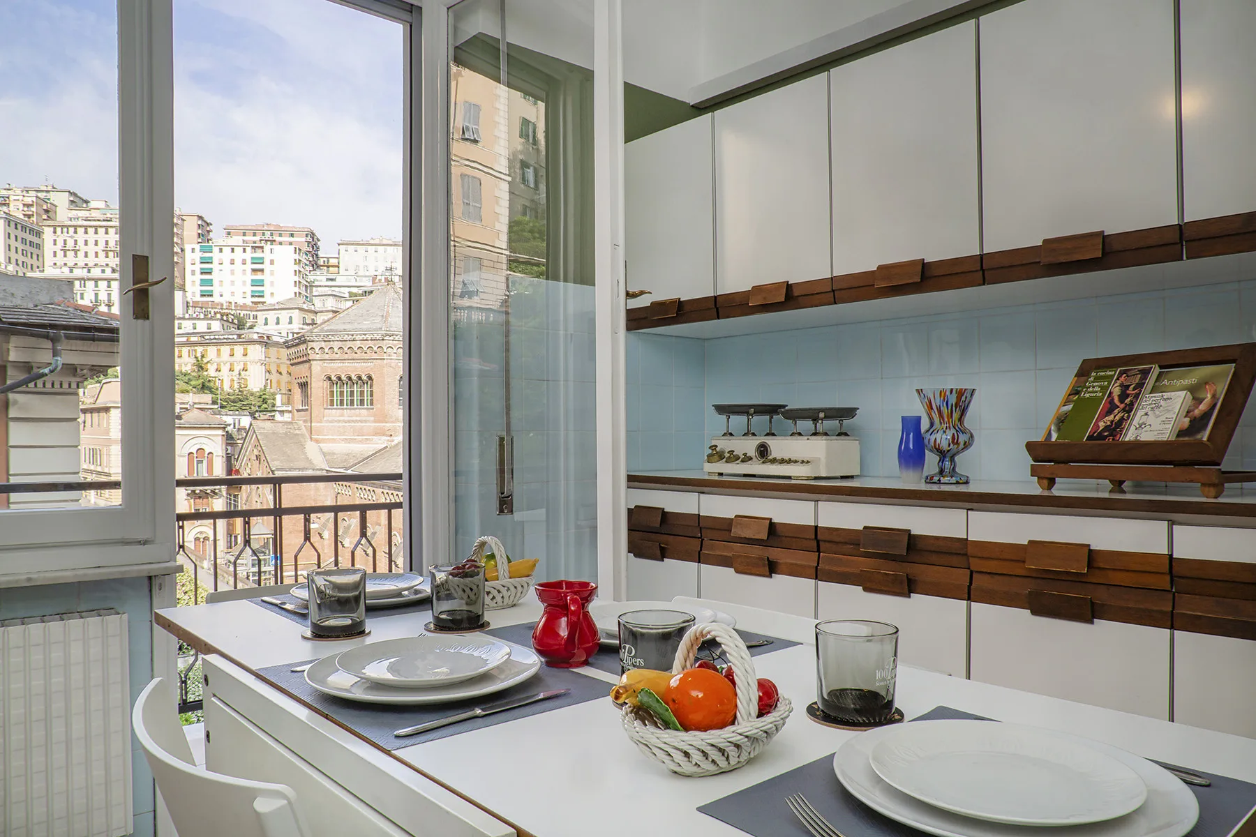 Una cocina luminosa con armarios blancos y una gran ventana con vistas a edificios de la ciudad.