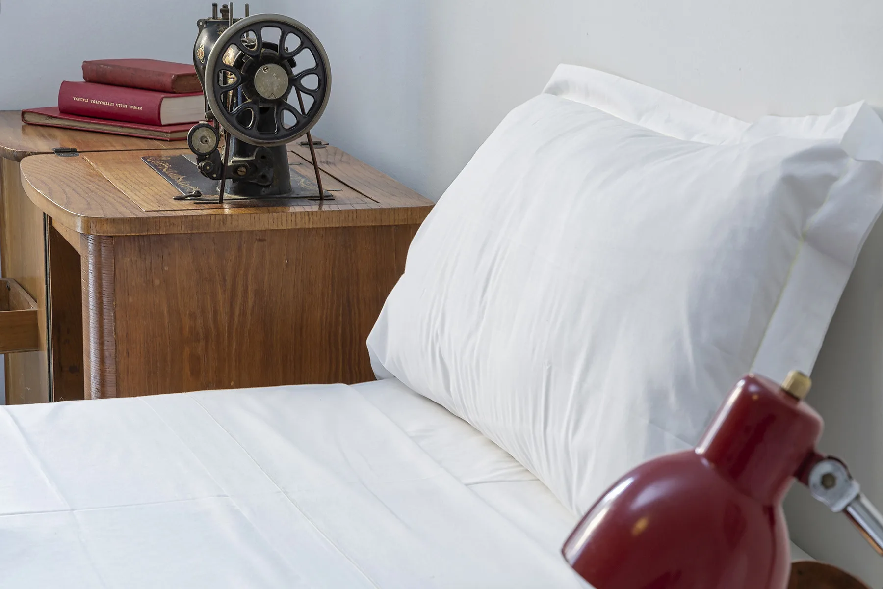 Un dormitorio con una cama blanca junto a una mesita de madera y una lámpara roja.