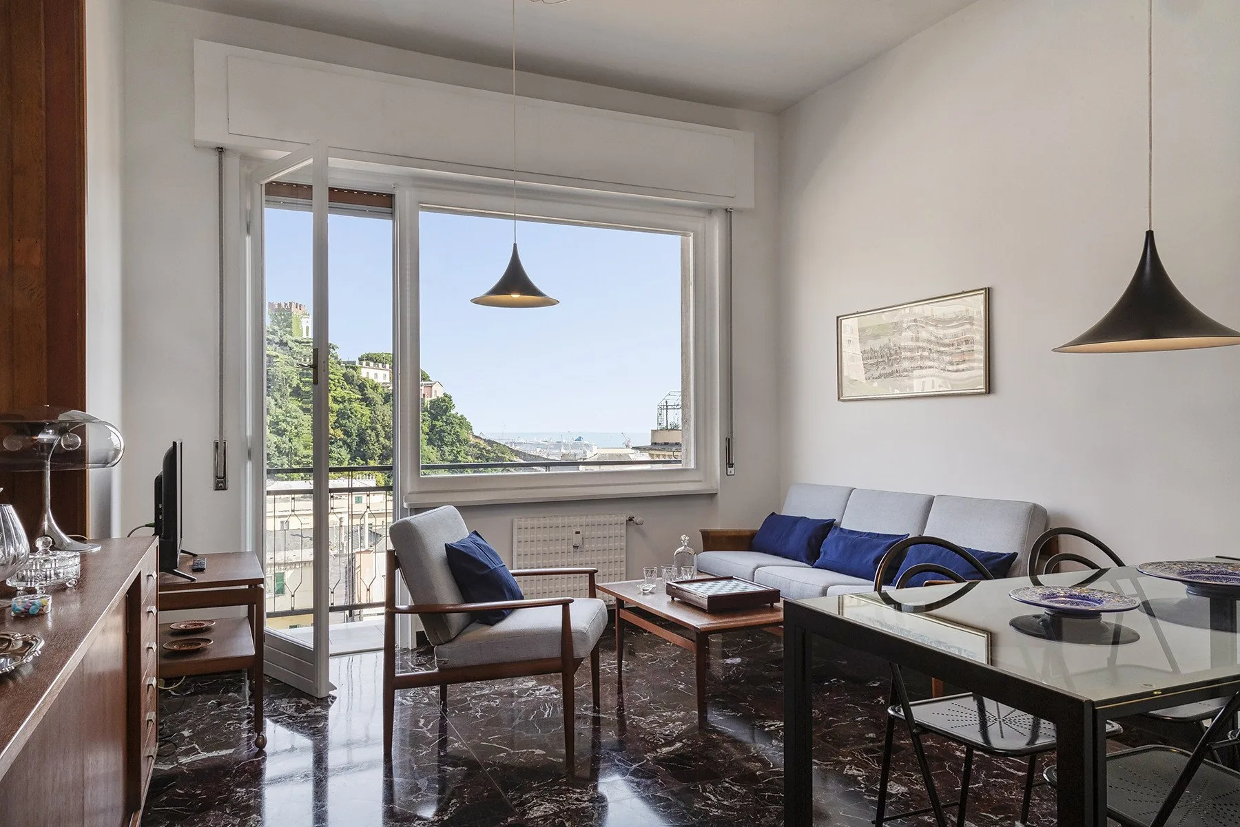 Una sala de estar con asientos y una gran ventana con vistas a vegetación y edificios.