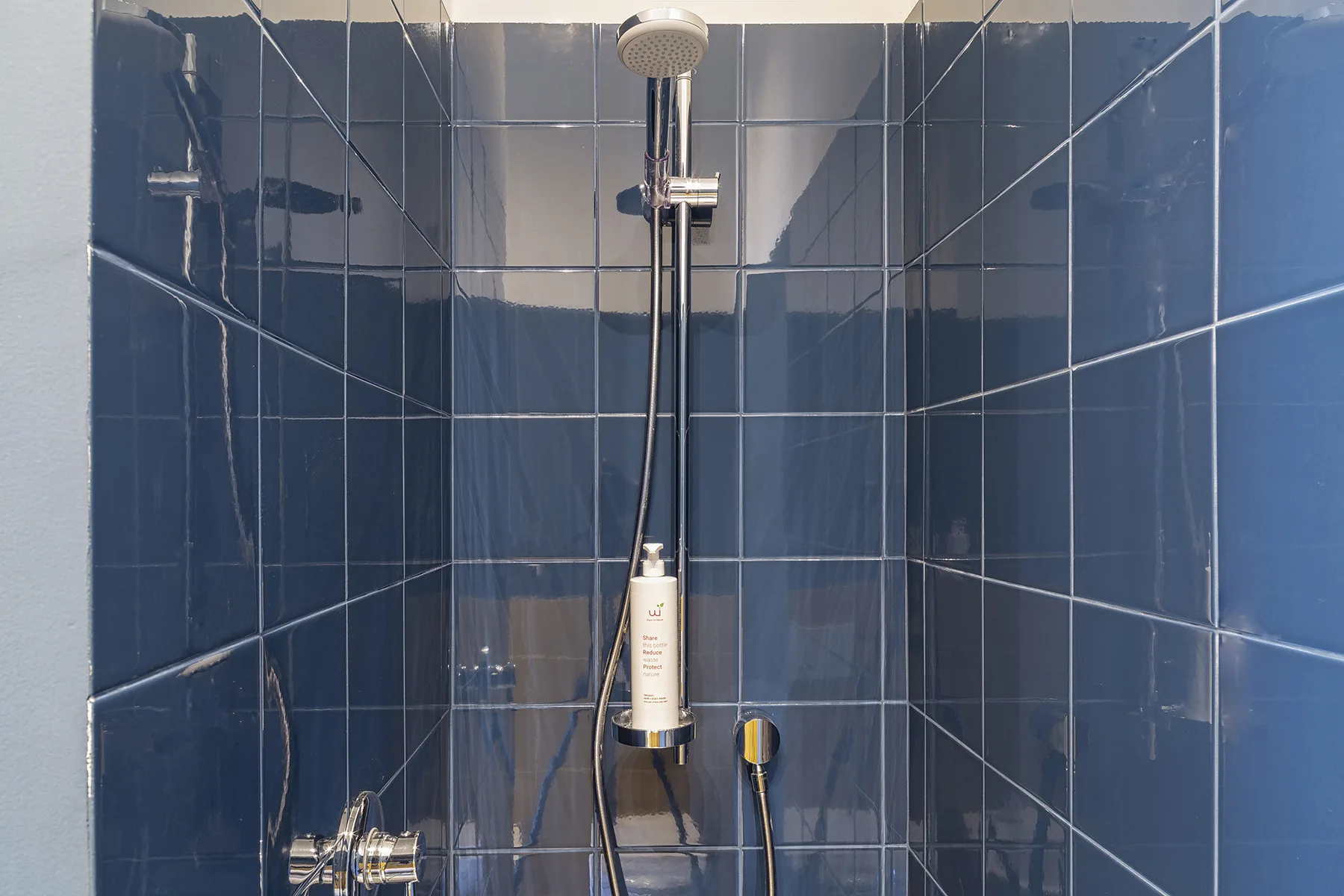 Una ducha con azulejos, un cabezal fijo y una ducha de mano.