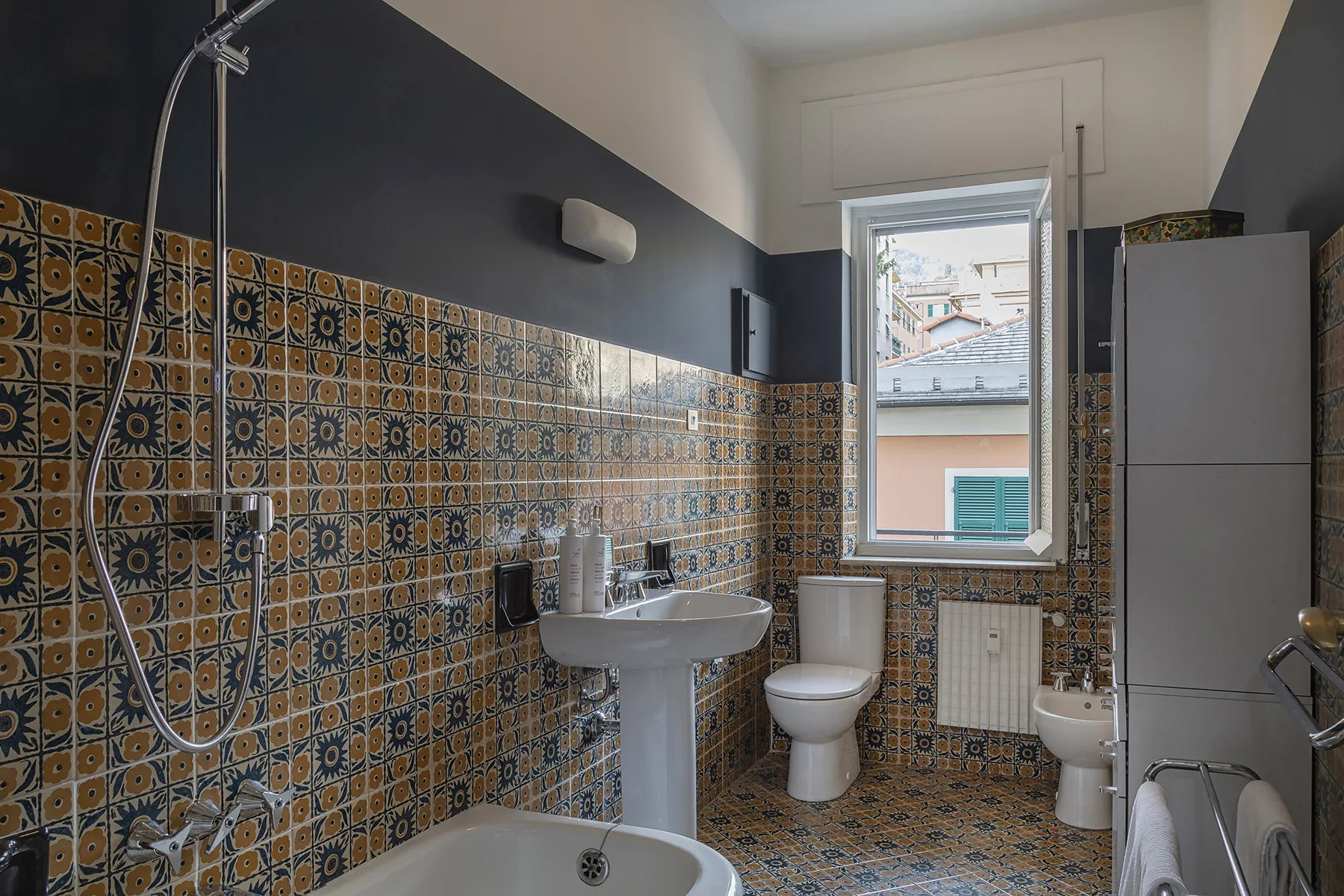 Un baño con azulejos, lavabo con pedestal, inodoro y ventana.