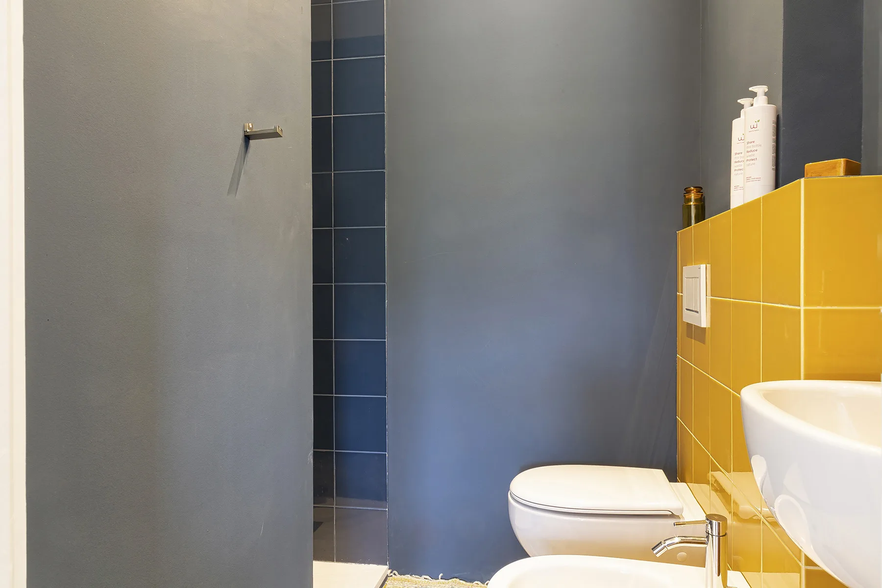 Un baño con inodoro, lavabo y una pared de azulejos amarillos.