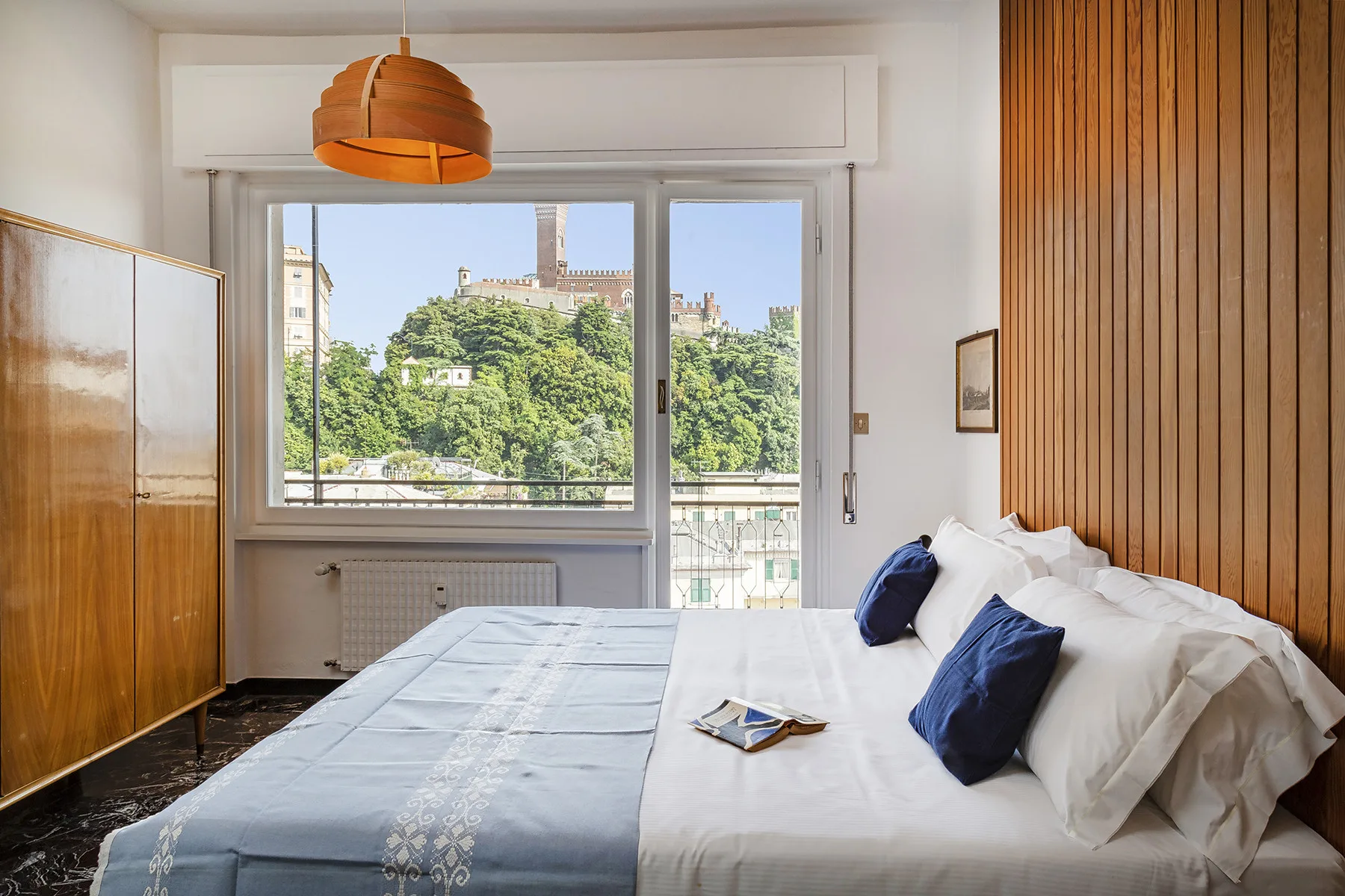 Un dormitorio con una cama junto a una ventana amplia con vistas a las copas verdes de los árboles.