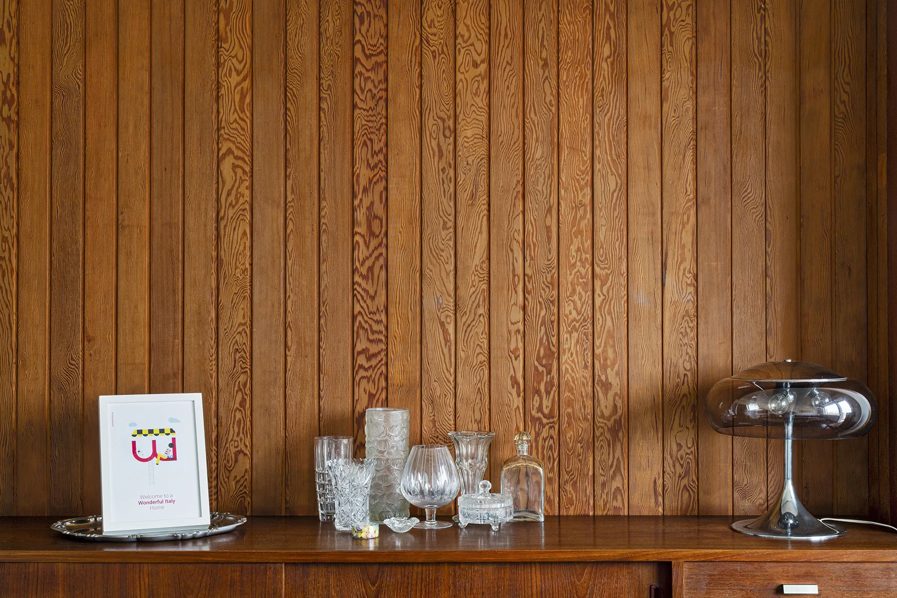 Una habitación con paneles de madera, cristalería y una lámpara sobre un aparador.