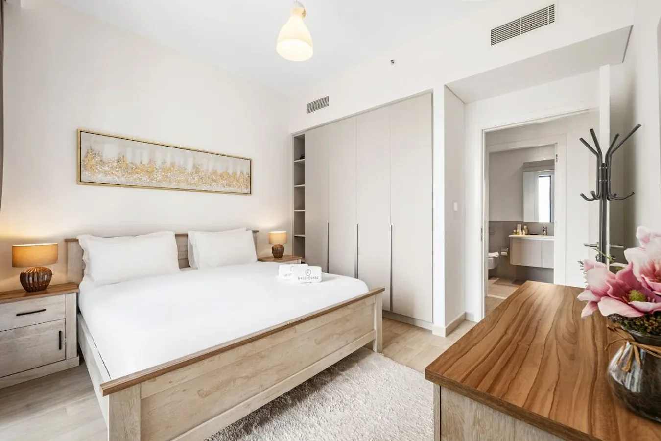 Un dormitorio luminoso con una cama blanca, armarios empotrados y un escritorio de madera.