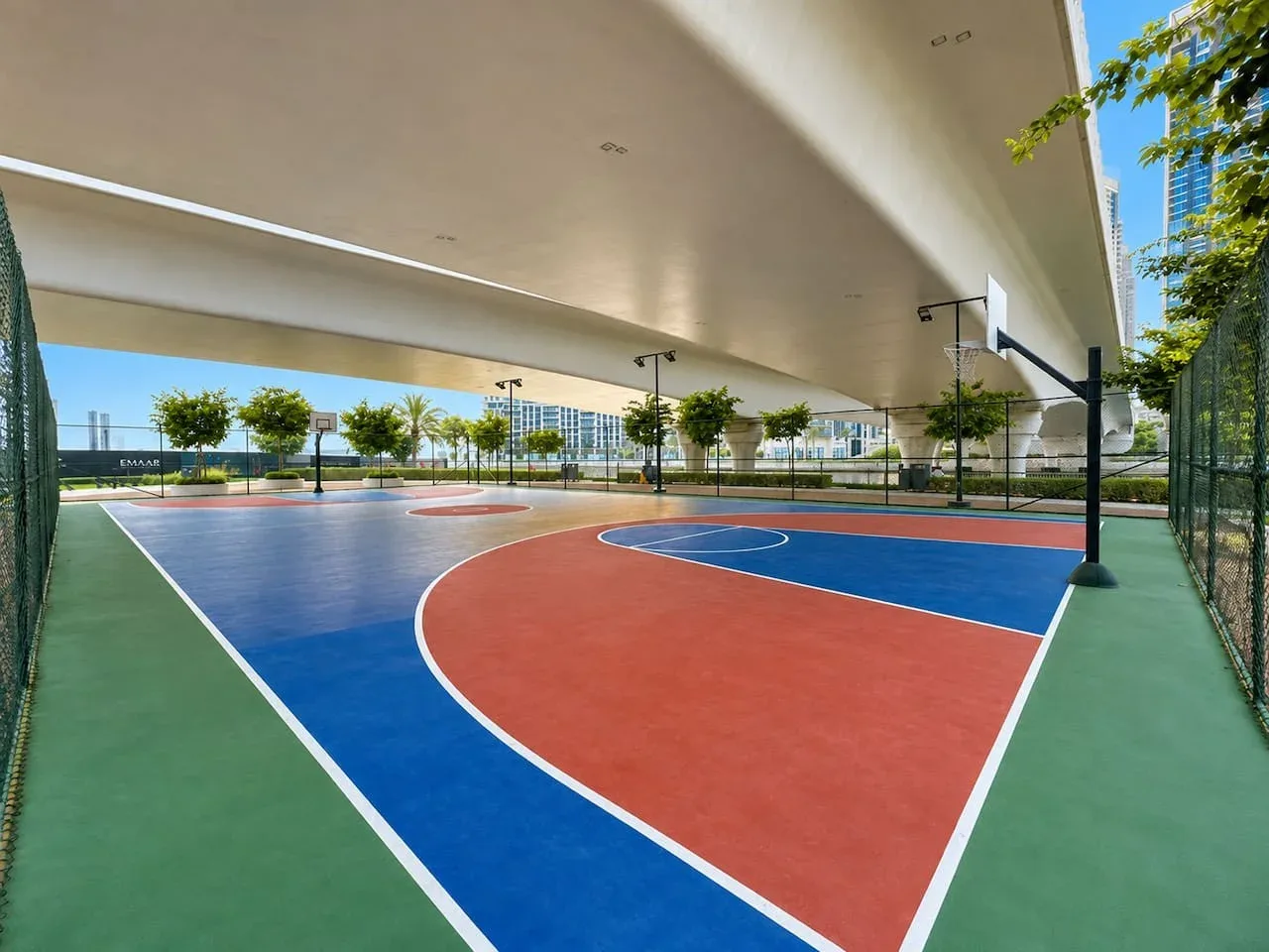 Una cancha de baloncesto al aire libre con superficies de colores bajo una estructura cubierta.