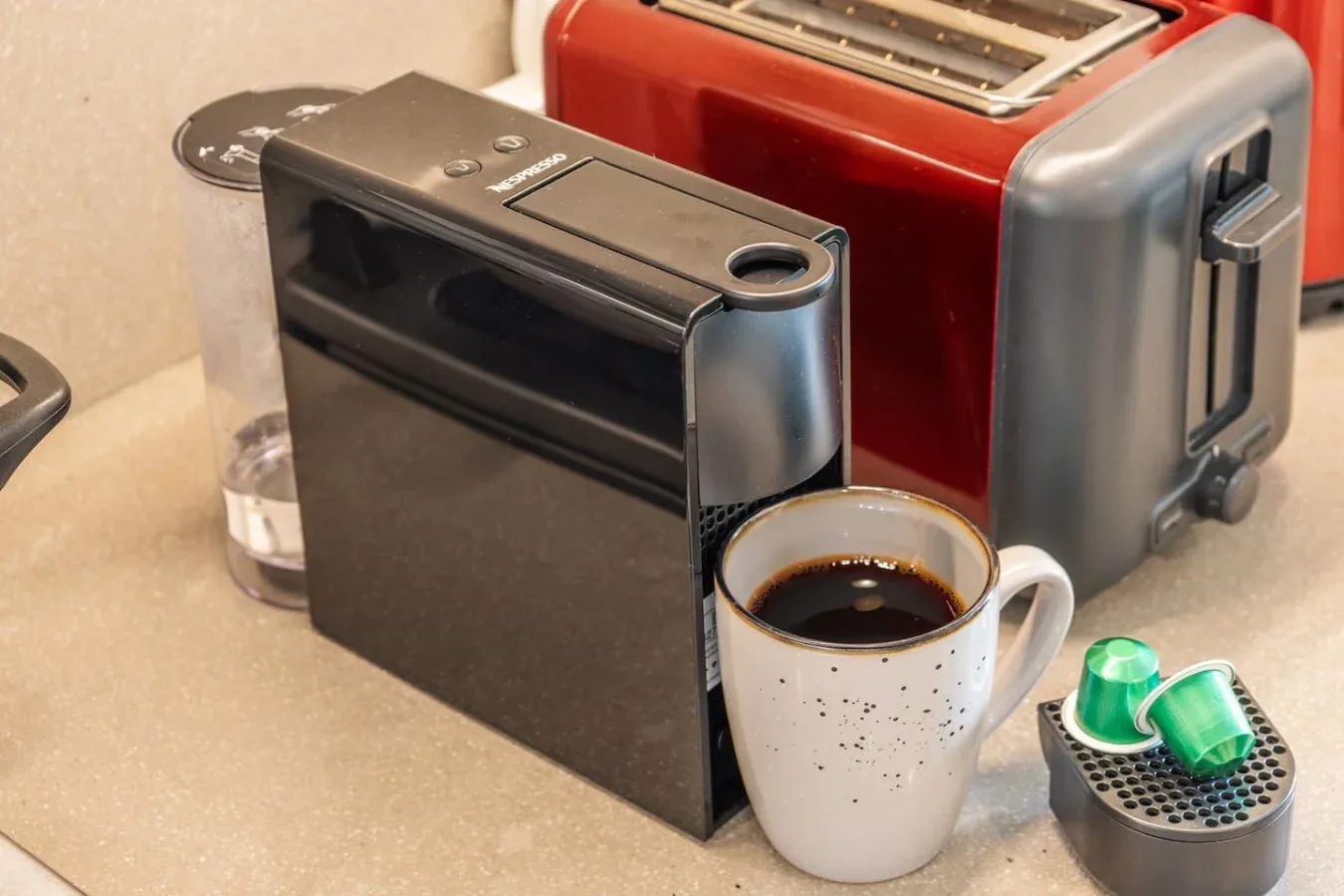 Una cafetera, una taza y una tostadora están juntas sobre una encimera de cocina.