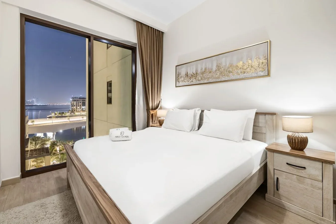 Un dormitorio luminoso con una cama grande, una mesita de noche y puertas de vidrio con vistas a la ciudad.