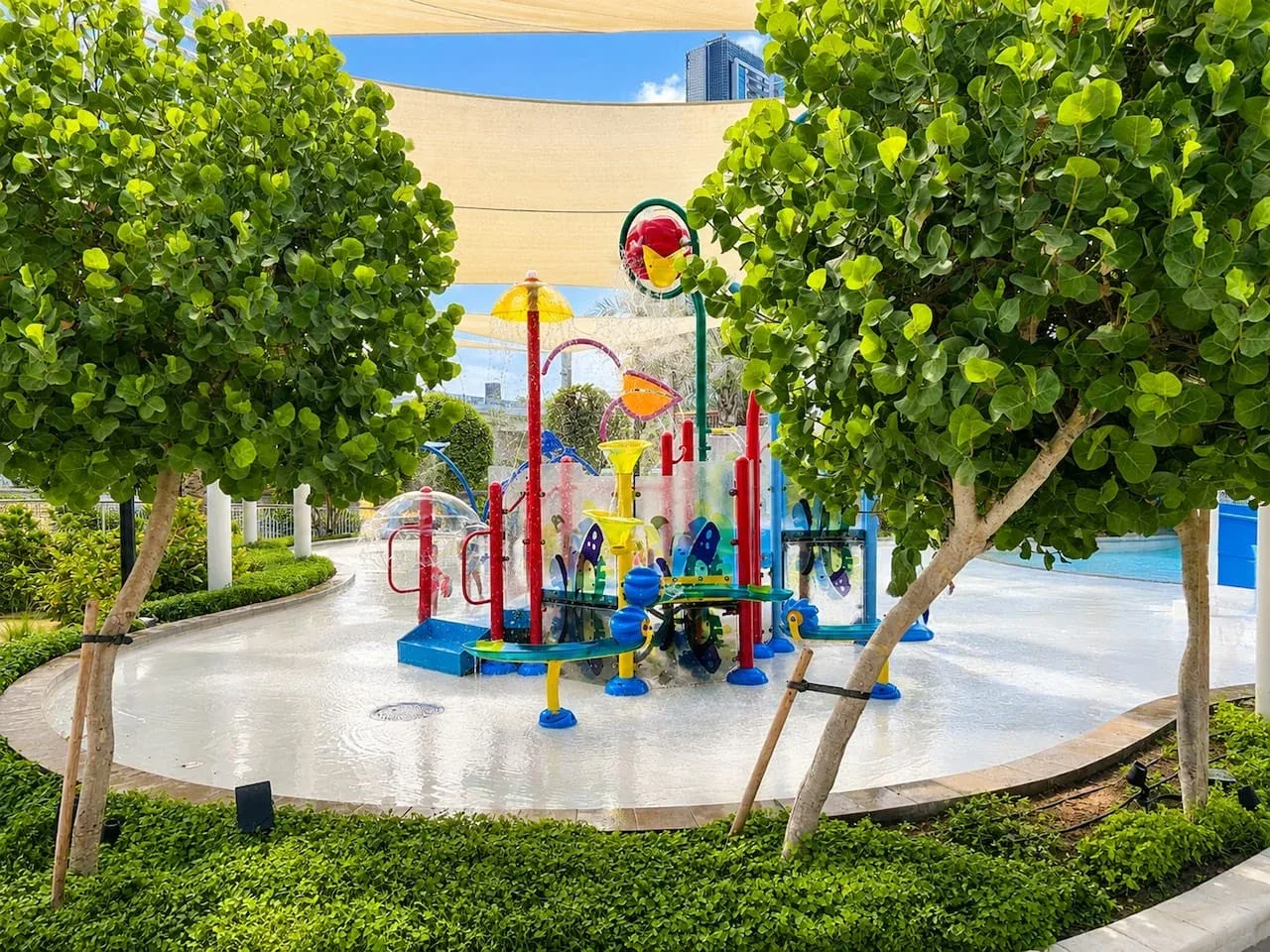 Un parque infantil colorido está en una zona pavimentada entre árboles frondosos.