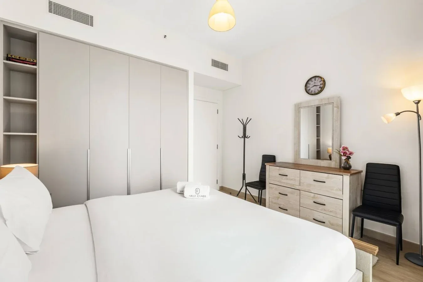 Un dormitorio luminoso con una cama blanca, una cómoda y un espejo.