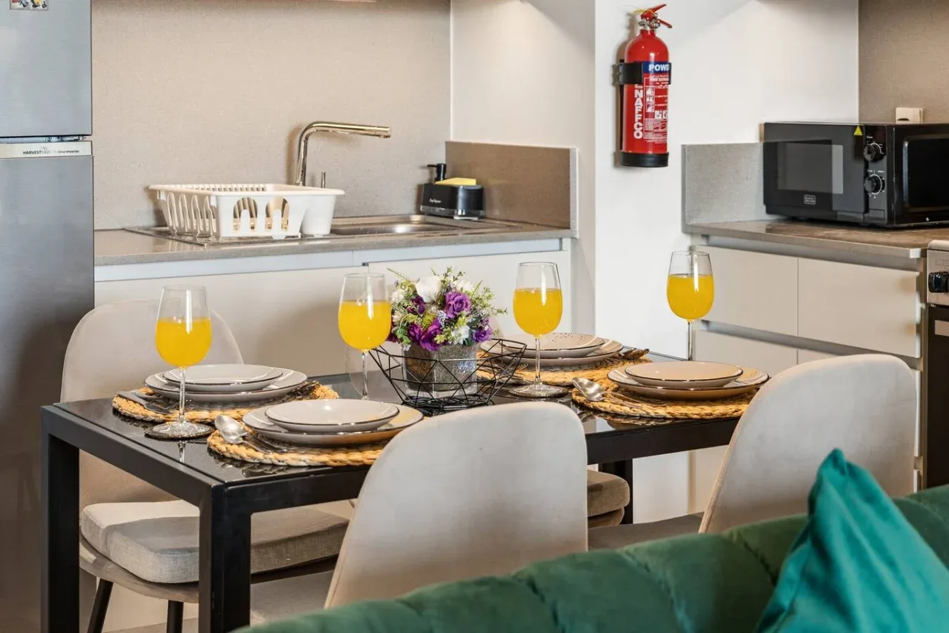 Una mesa de comedor puesta con platos y bebidas está frente a una cocina.