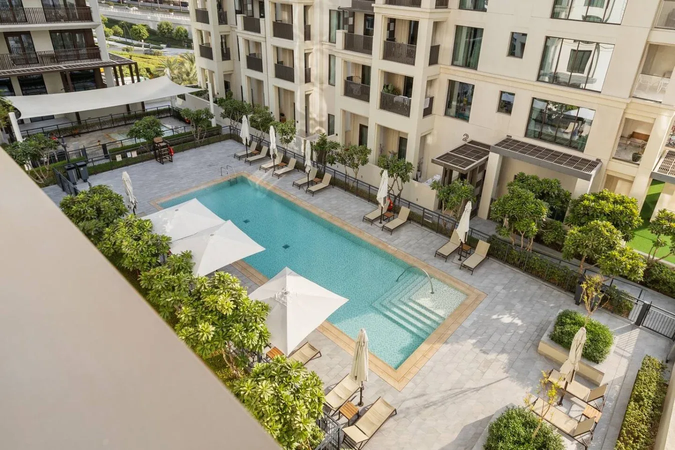 Una piscina al aire libre con asientos y sombrillas está rodeada de edificios de apartamentos.
