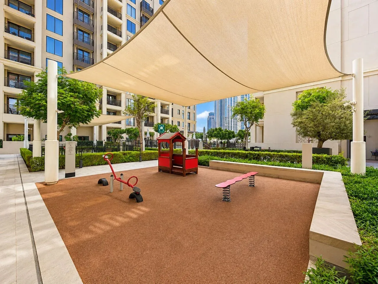 Un área de juegos al aire libre con sombra, una estructura pequeña y balancines.