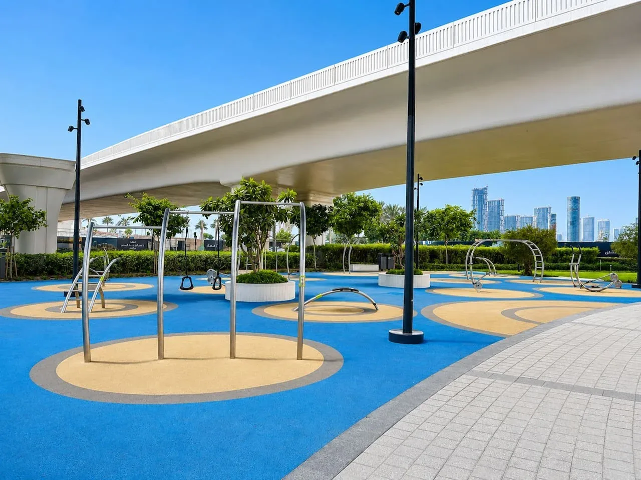 Un colorido parque infantil al aire libre con estructuras para trepar está bajo una vía elevada.
