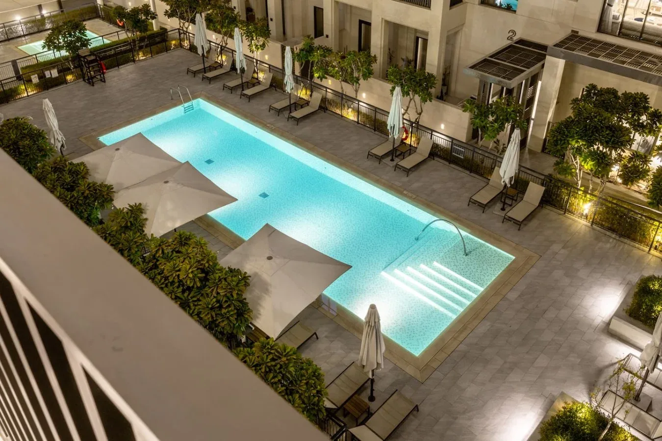 Una piscina exterior iluminada está rodeada de asientos de descanso y sombrillas.