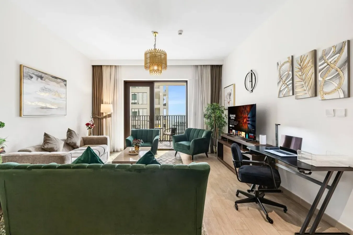 Una sala luminosa con asientos verdes, un televisor y un escritorio junto a las puertas del balcón.