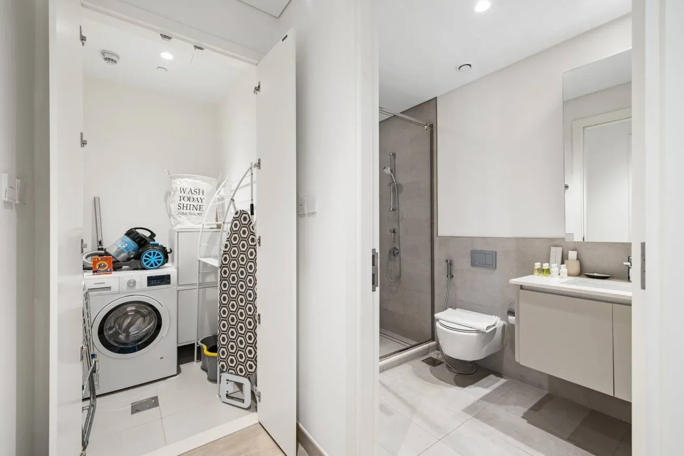Un baño luminoso con zona de lavandería, lavadora, ducha, inodoro y lavabo.