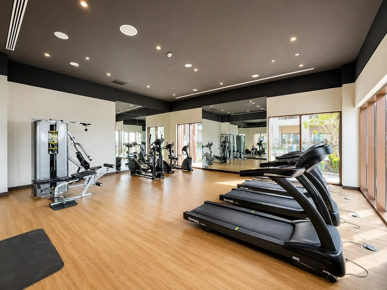 Un gimnasio con máquinas de ejercicio y cintas de correr frente a paredes con espejos.