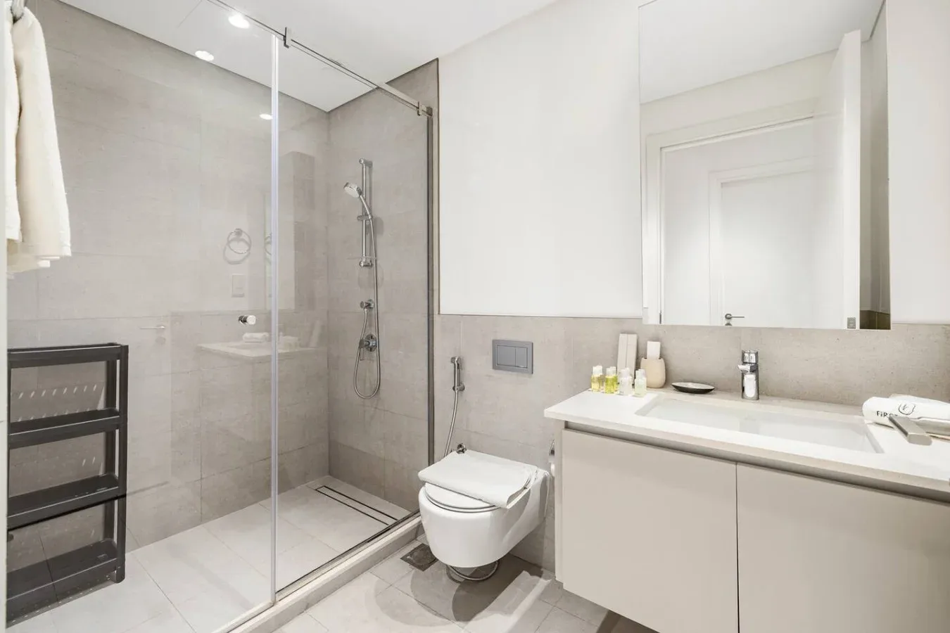 Un baño luminoso con ducha de vidrio, inodoro suspendido y lavabo con mueble.
