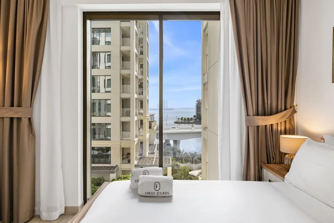 Un dormitorio con la cama tendida y una ventana con vistas a edificios cercanos y al agua.
