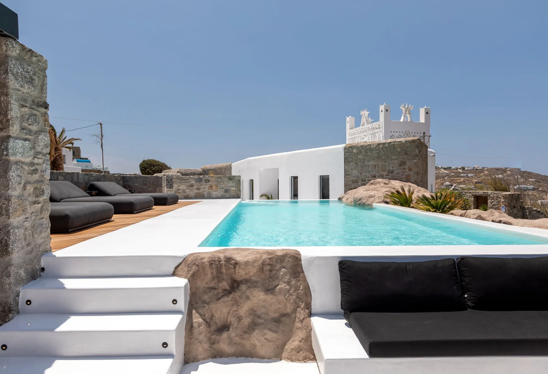 Una piscina en la azotea junto a un edificio blanco, con asientos oscuros en la terraza.