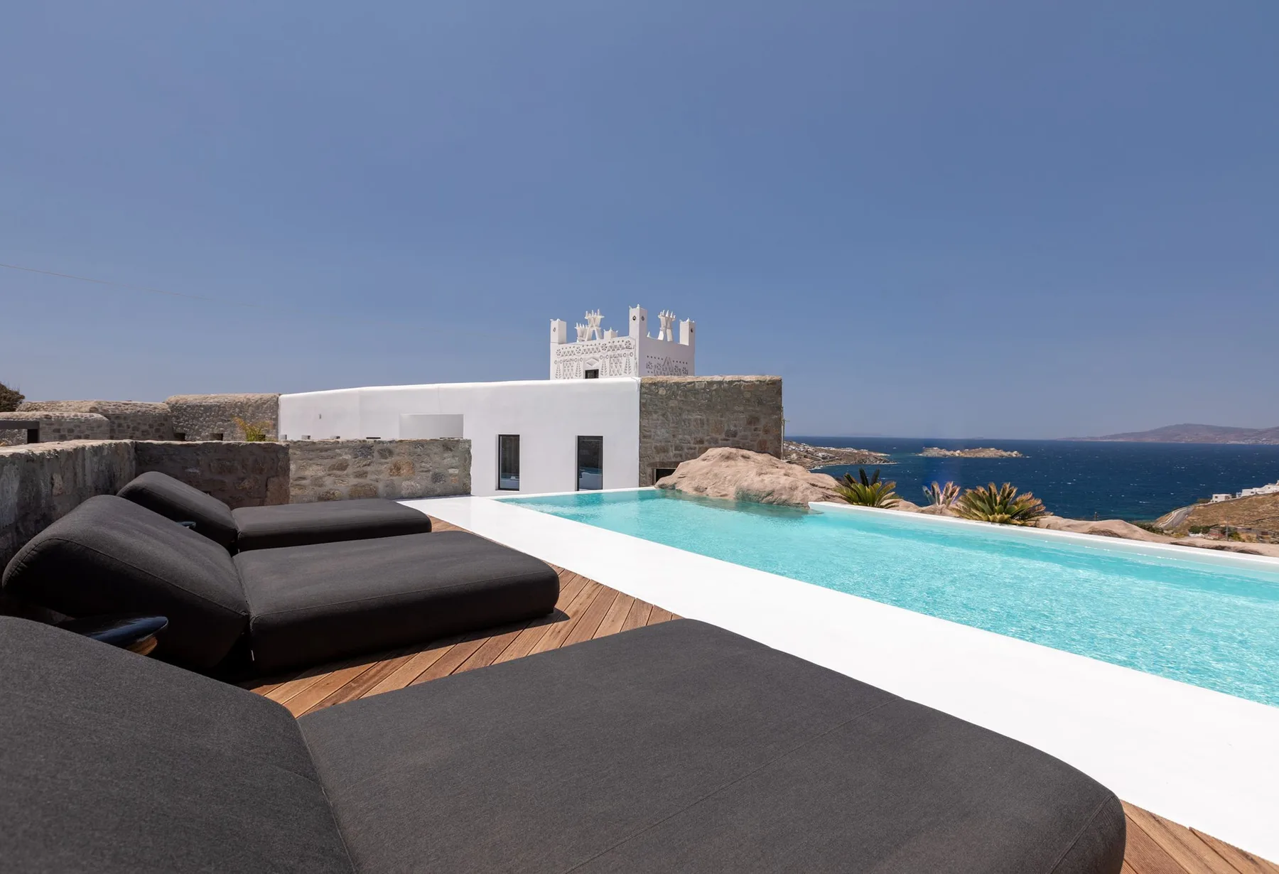 A modern terrace features a turquoise pool, dark lounge seating, and a sea view.