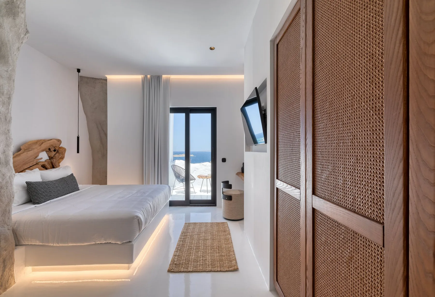 Un dormitorio luminoso con una cama, puertas de armario trenzadas y vistas al mar por las puertas de cristal.