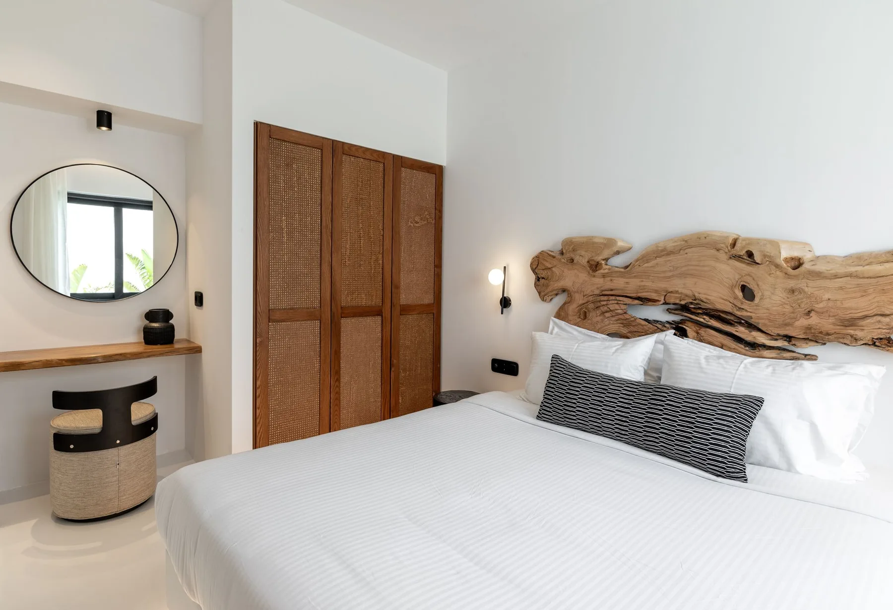 Un dormitorio luminoso con ropa de cama blanca y un cabecero de madera tallada.