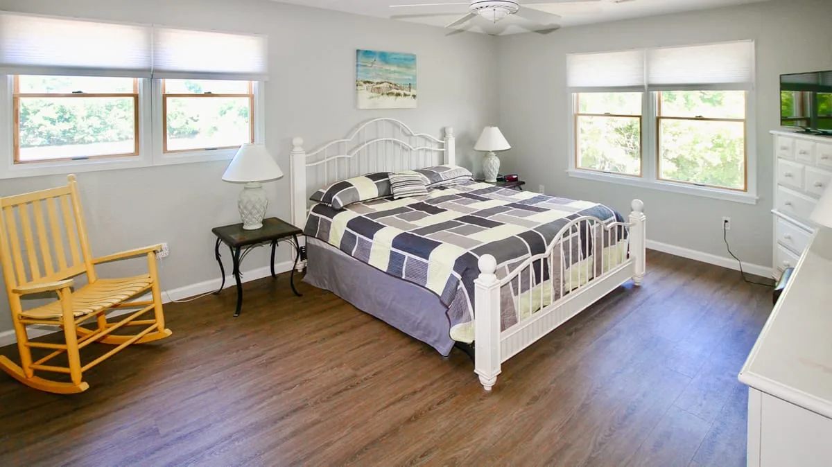 Un dormitorio luminoso con una cama blanca, ropa de cama estampada y piso de madera.