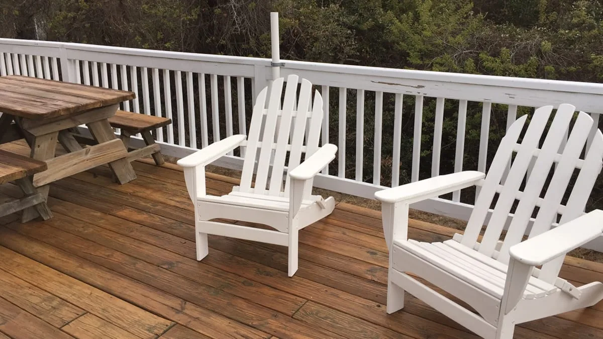 Una terraza de madera con asientos blancos y una mesa de picnic da a los árboles.