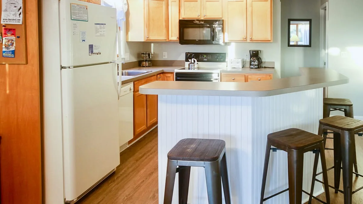 Una cocina con refrigerador blanco, gabinetes de madera y una barra con taburetes.