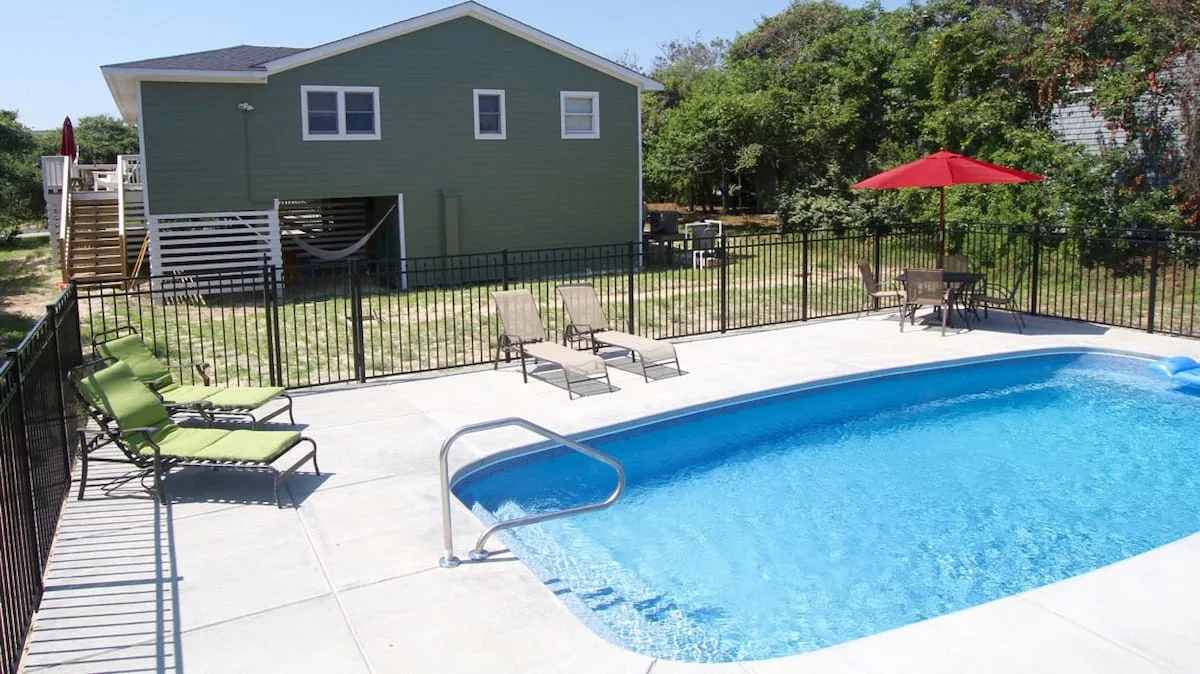 Una piscina al aire libre está junto a un patio cercado con asientos reclinables.
