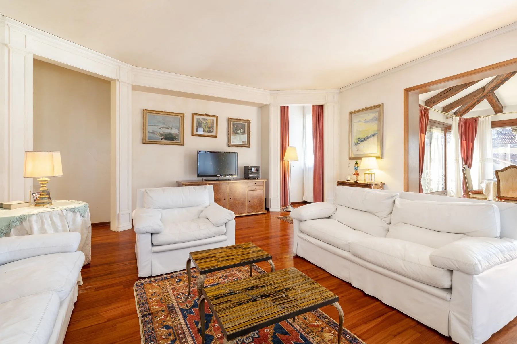 A bright living room with pale seating, framed artwork, and a television.